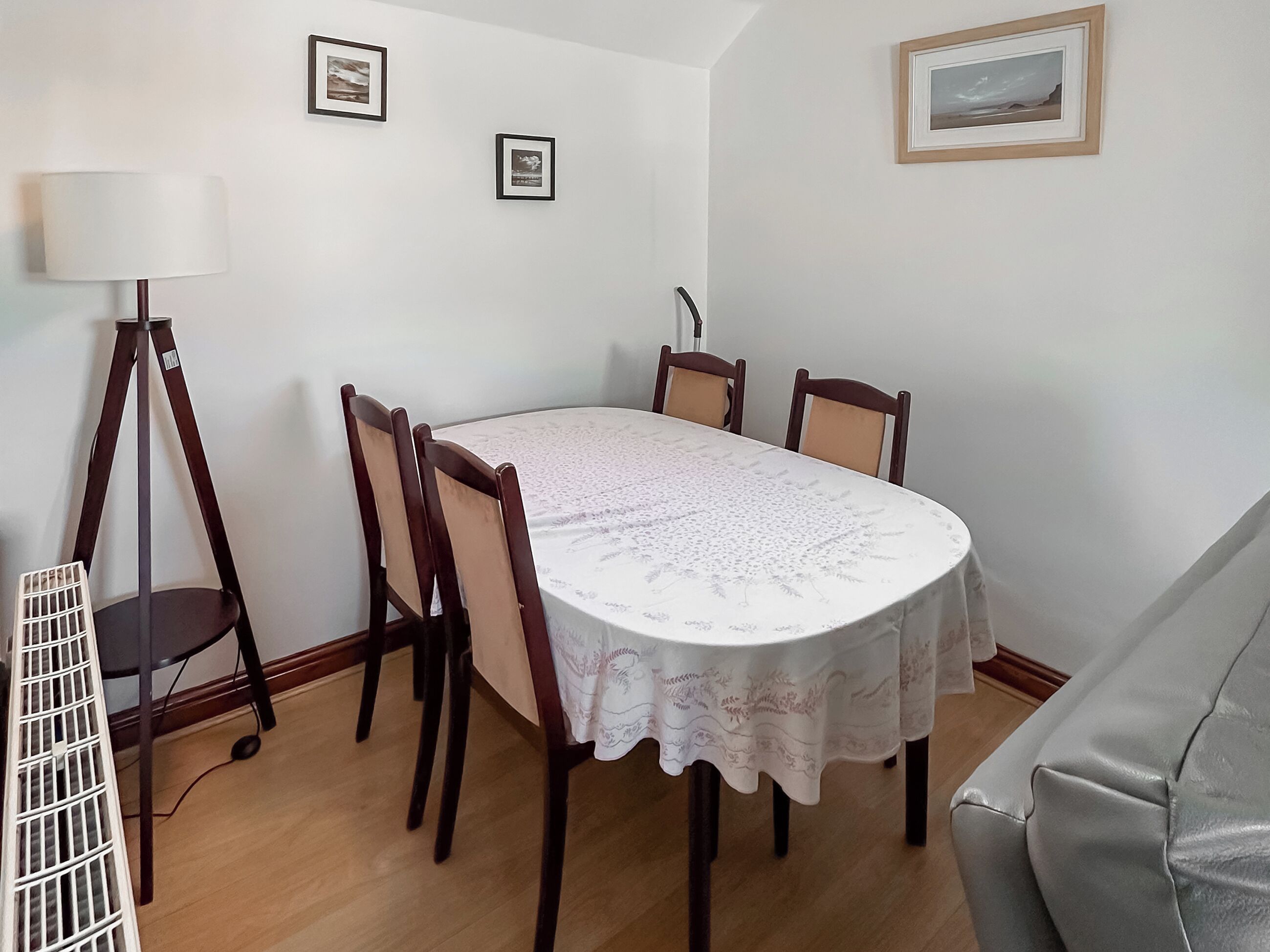 Un área de comedor con una mesa redonda, cuatro sillas, una lámpara de pie y dos cuadros en la pared.