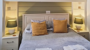 Un lit bien fait, avec une tête de lit, deux tables de chevet avec des lampes et une armoire au-dessus.