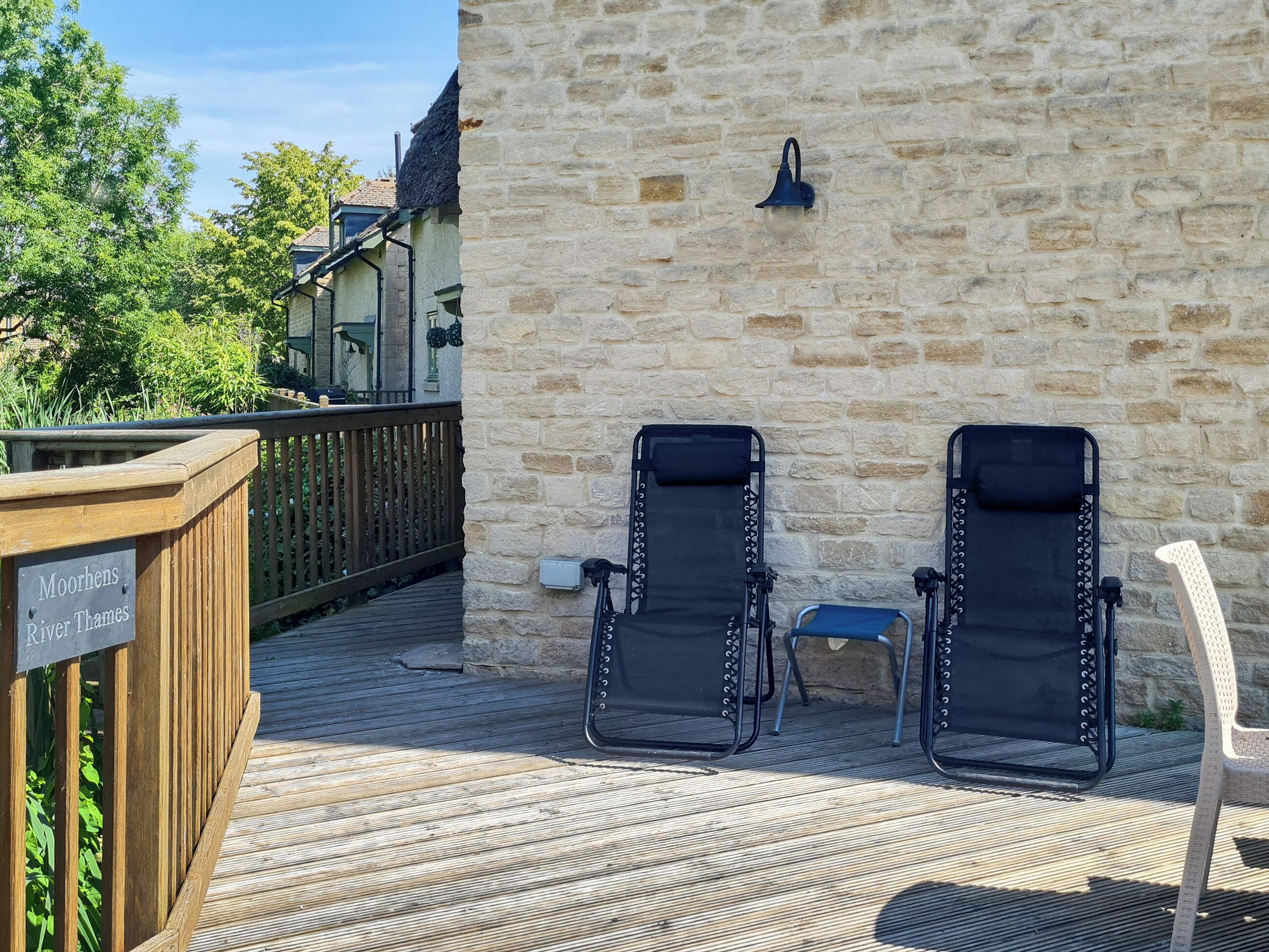 A wooden deck with two black lounge chairs and a sign indicating the location as Moorhens River Thames.