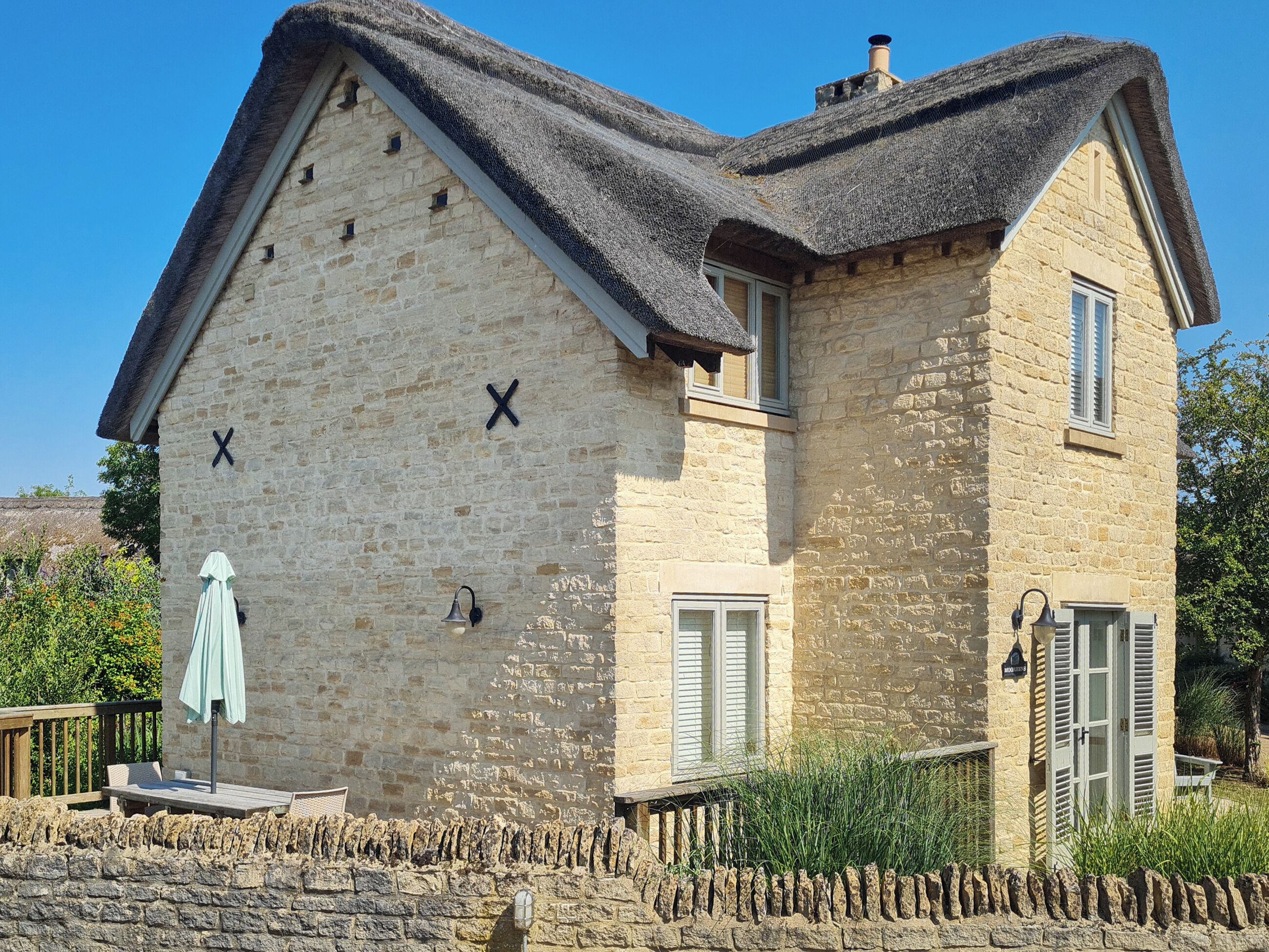 A stone building with a steeply pitched roof, a wooden deck, and a stone wall.