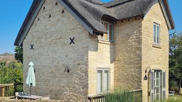 A stone building with a steeply pitched roof, a wooden deck, and a stone wall.