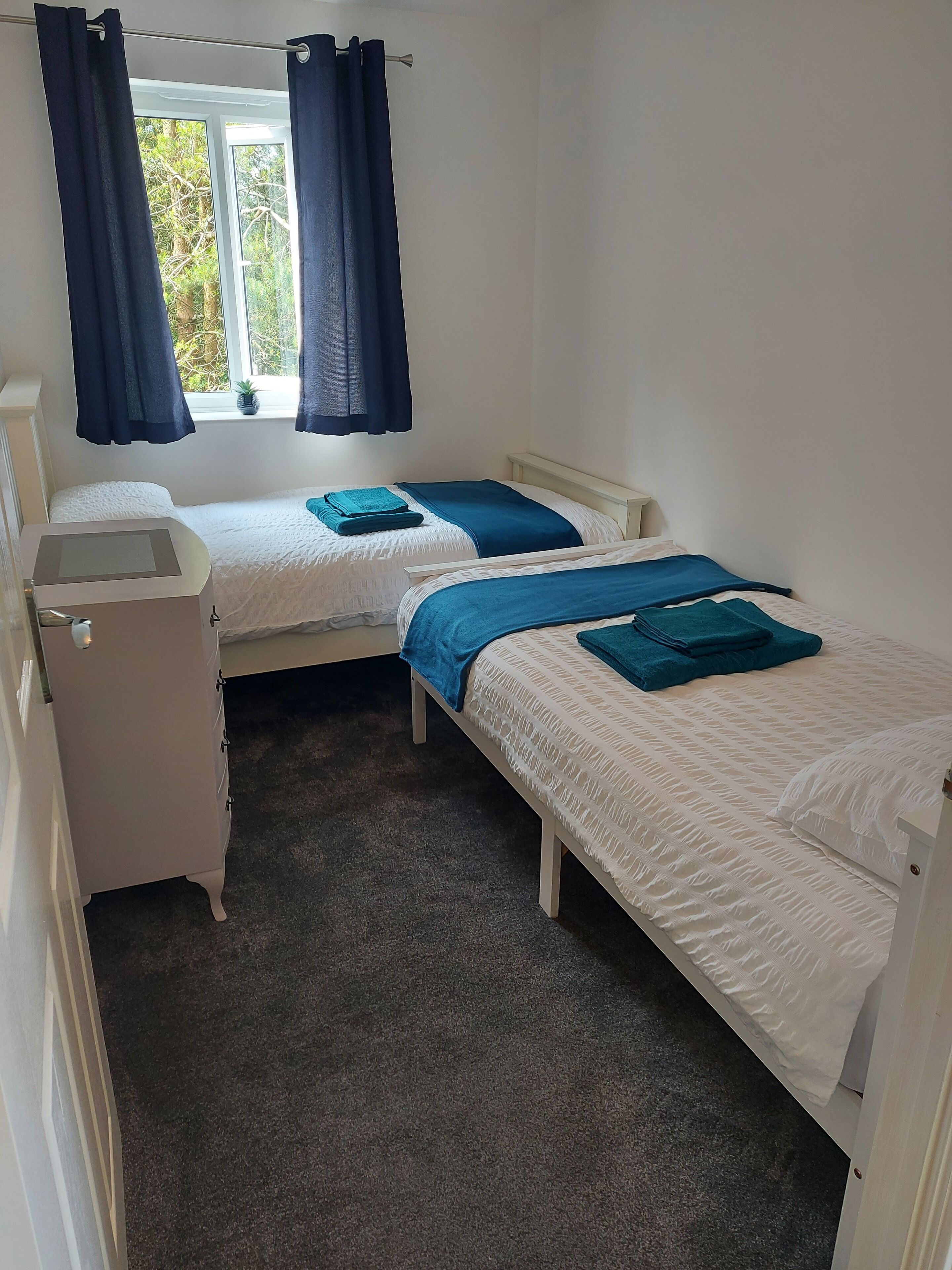 A bedroom with two beds, a desk, and a window with curtains.