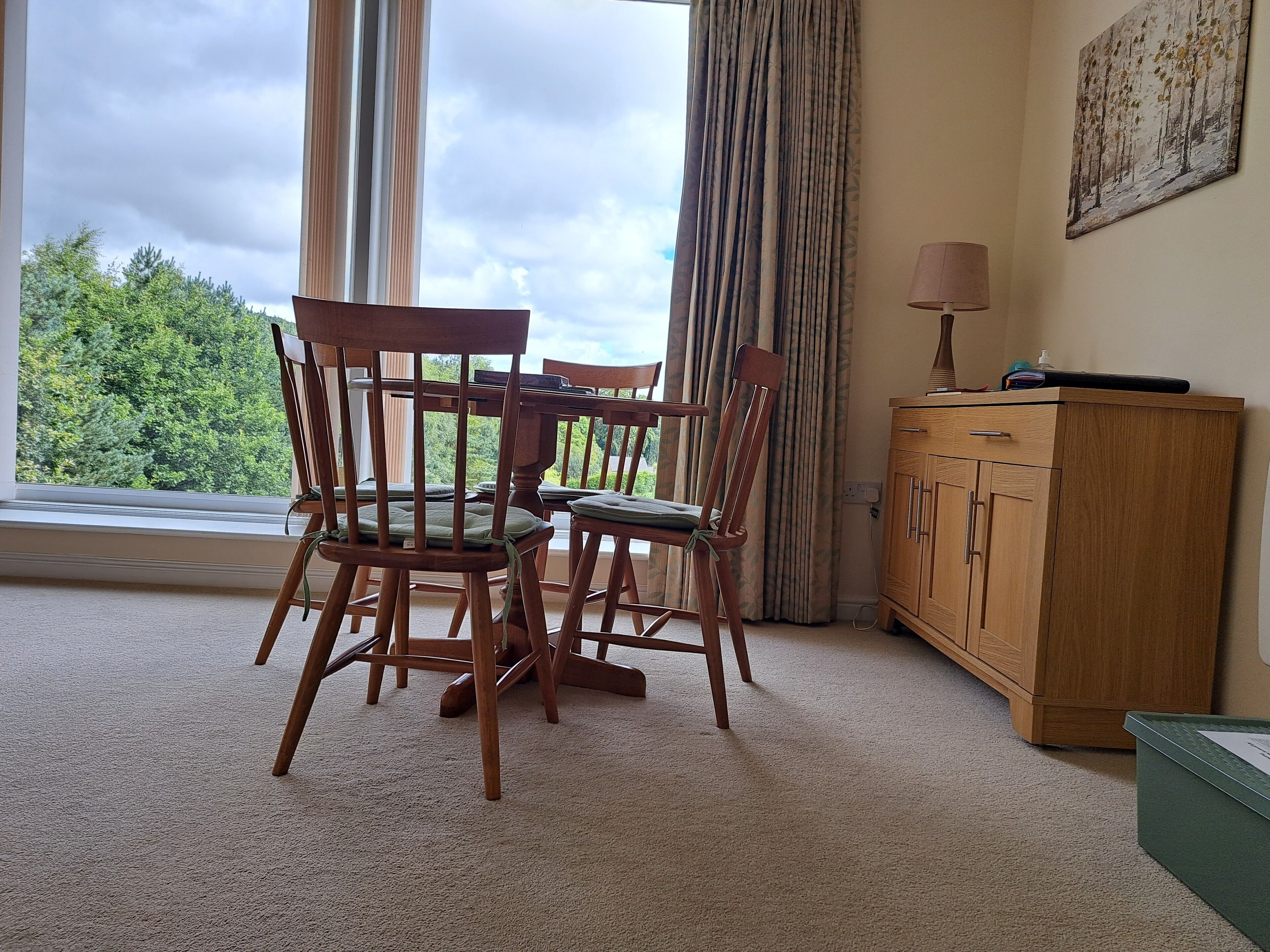 A room with a dining table and chairs, a wooden cabinet, and a window with curtains.