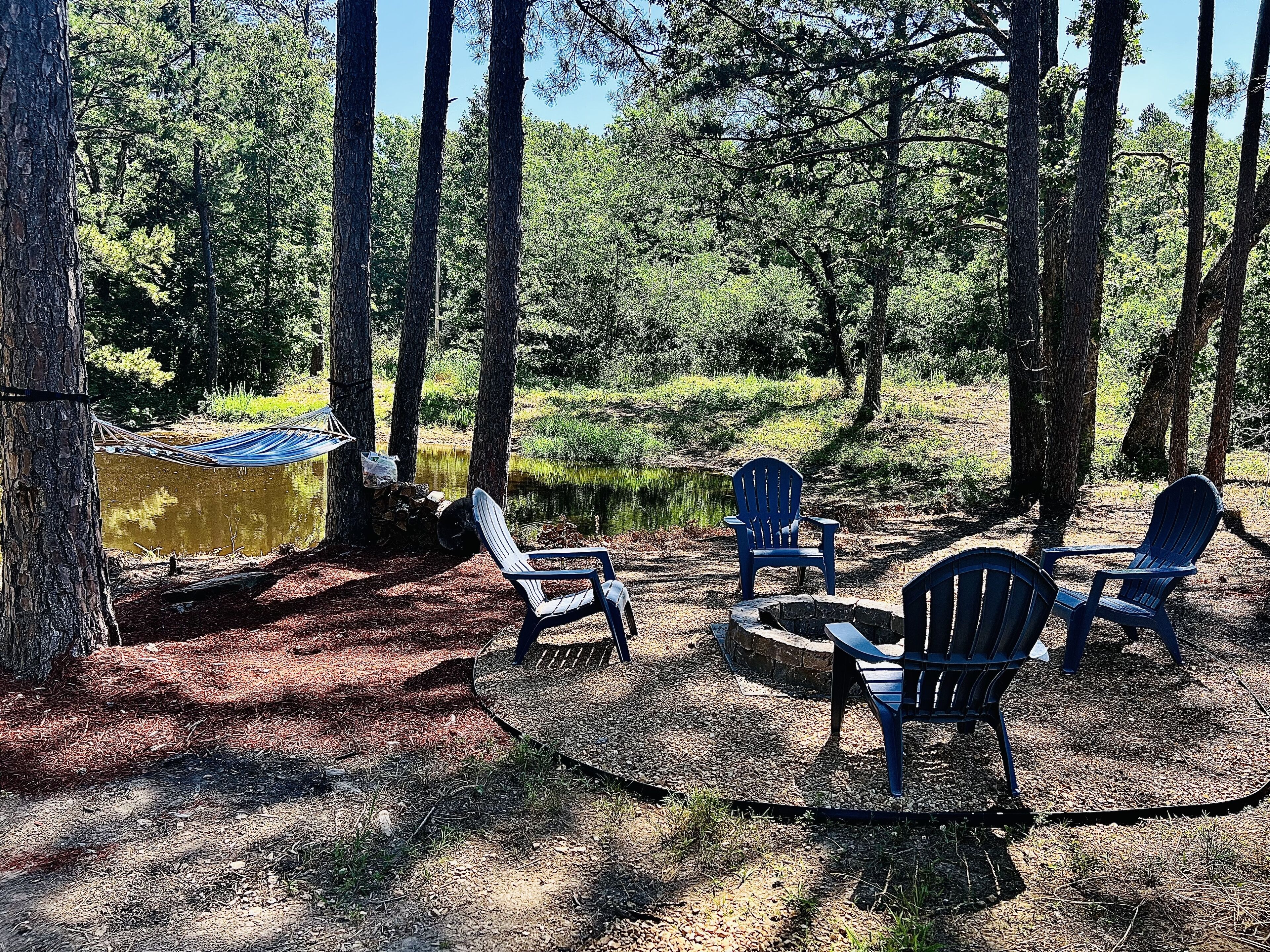 Un camping con una hamaca, un pozo para fuego y varias sillas Adirondack.