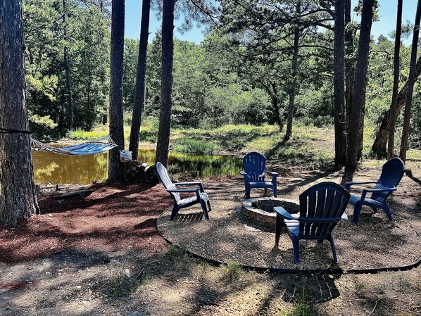 A campsite with a hammock, a fire pit, and several Adirondack chairs.