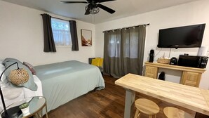 Una habitación pequeña con cama, un escritorio con computadora, televisor y ventilador de techo.