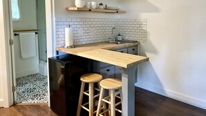 Una cocina con encimera de madera, dos taburetes, un fregadero y un refrigerador.