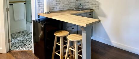 A kitchen with a wooden countertop, two stools, a sink, and a refrigerator.