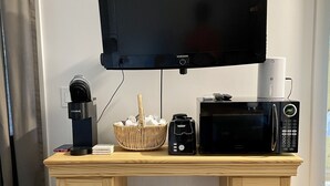 Un escritorio de madera con televisor, cafetera, microondas y una cesta de huevos.
