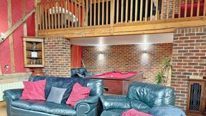 A living room with a pool table, leather sofas, a wooden coffee table, and a brick wall.