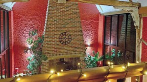 A room with a brick fireplace, a clock, and wooden beams.