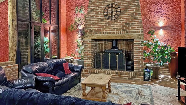A cozy patio area with a brick fireplace, leather sofa, and a wooden table.
