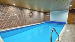 An indoor swimming pool with a brick wall, a ship's wheel decoration, and a blue pool edge.