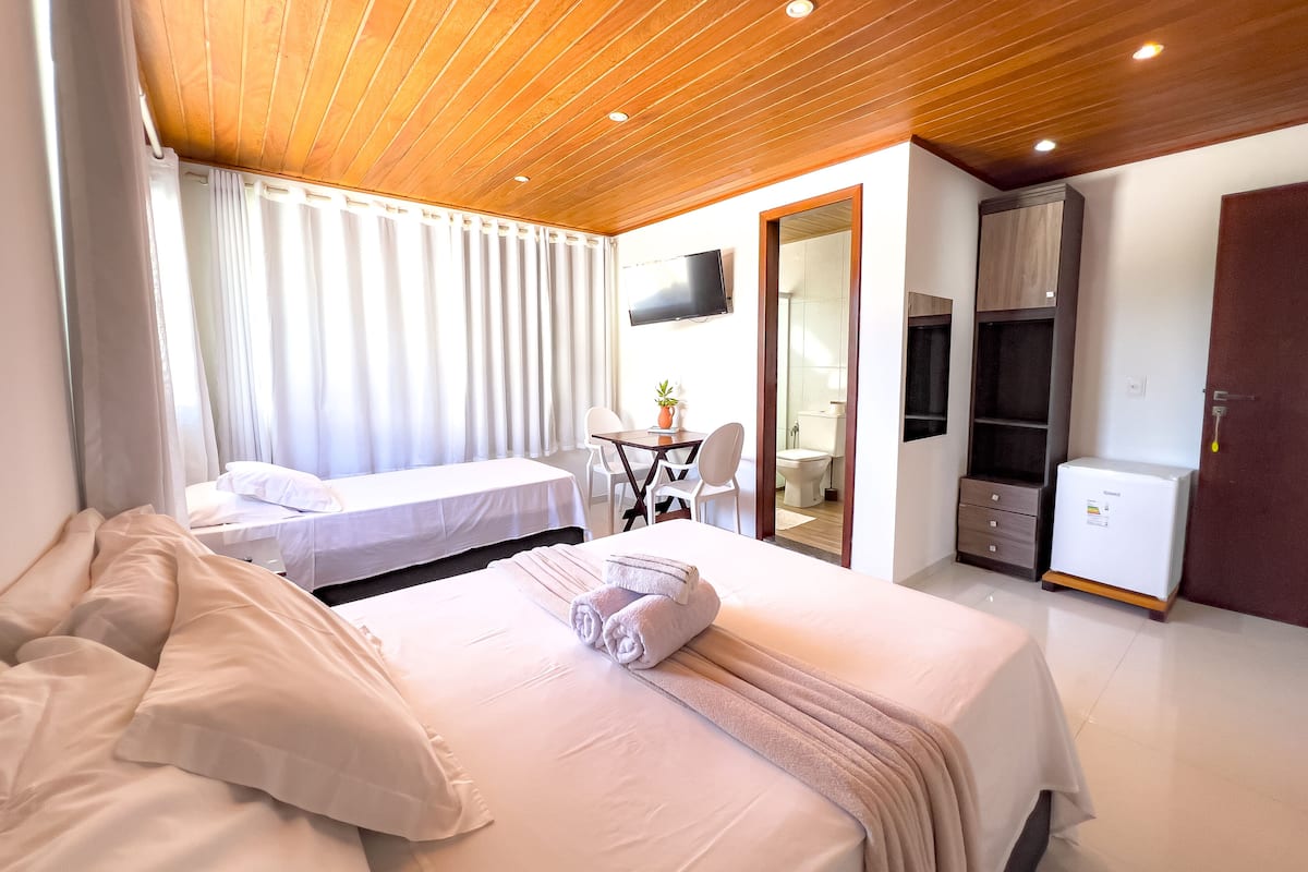 Ein Hotelzimmer mit Holzboden, zwei Betten, einem Schreibtisch mit Stuhl, einem Fernseher und einem Kühlschrank.