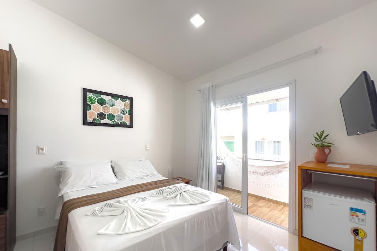 Ein Hotelzimmer mit einem Bett, einem Fernseher, einem kleinen Kühlschrank und einem Fenster mit Vorhängen.