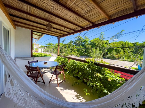 A covered patio with a round table and chairs, surrounded by lush greenery and a hammock. - Pousada Linda Flor (Cairu)