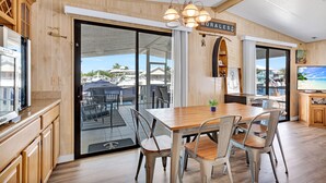 A modern kitchen with wooden cabinetry, a dining area with a wooden table and metal chairs, and a view of the outdoor patio area. - Paradise on main canal with spectacular sunset (Key Largo)