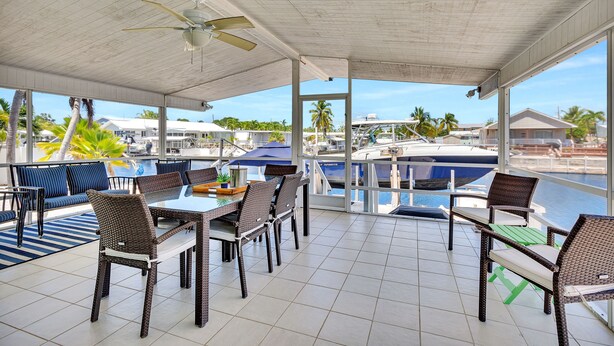 A covered outdoor seating area with a table and chairs, overlooking a marina with boats and palm trees. - Paradise on main canal with spectacular sunset (Key Largo)