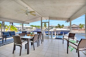 A covered outdoor seating area with a table and chairs, overlooking a marina with boats and palm trees. - Paradise on main canal with spectacular sunset (Key Largo)