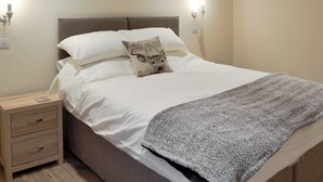 A neatly made bed with white linens and a gray blanket, a wooden nightstand with drawers, and wall-mounted sconces. - 2 bedroom accommodation in Alkham, near Dover (Alkham, near Dover)
