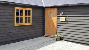 A building with a dark exterior, a wooden door, a window with yellow framing, and a small potted plant. - 2 bedroom accommodation in Alkham, near Dover (Alkham, near Dover)