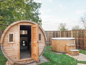 A wooden cabin with an open door, a hot tub, and a small outdoor seating area. - Meadowsweet Cottage-UKC2458 (Swardeston, near Mulbarton)