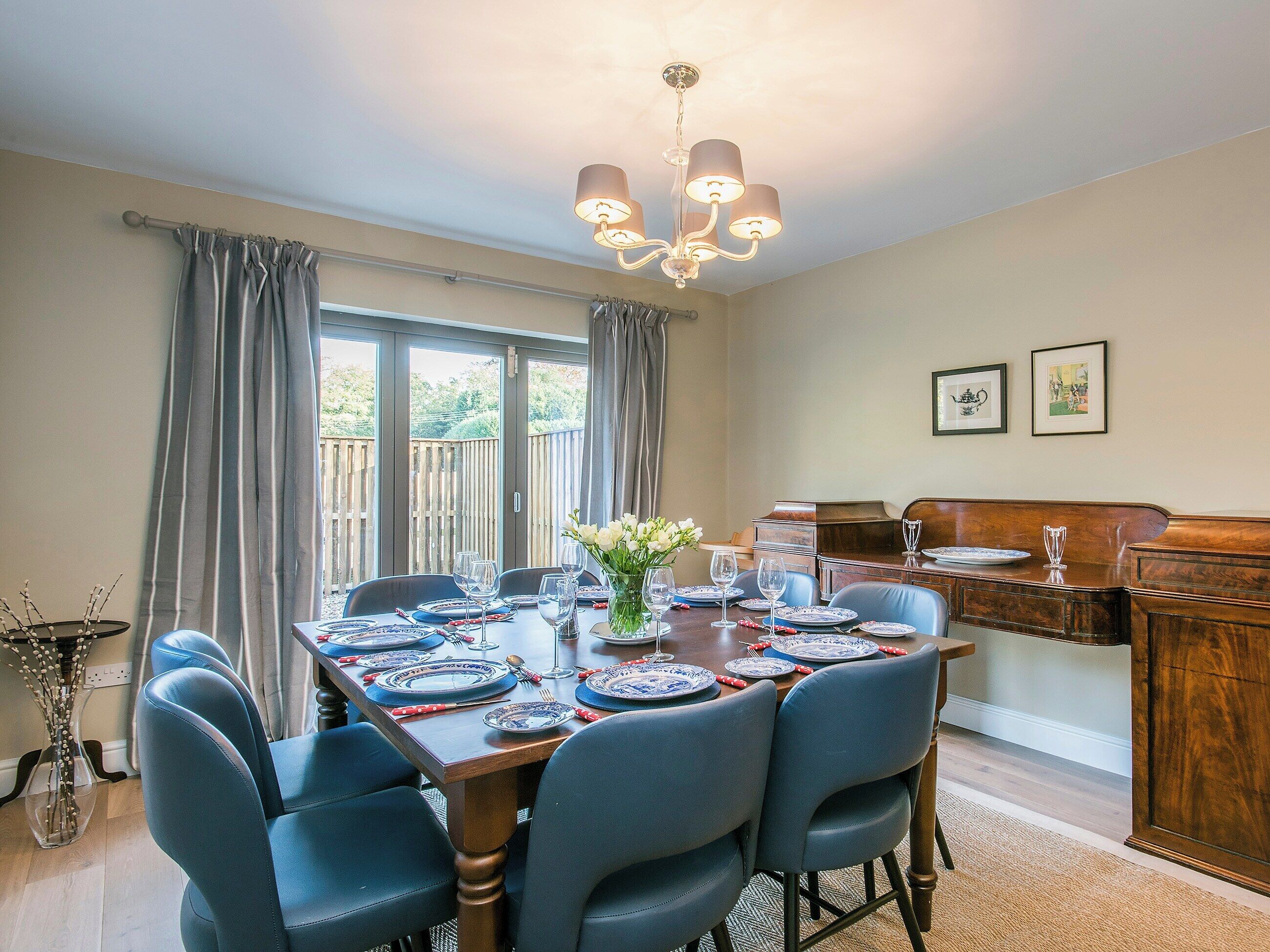 A dining room with a wooden table set for four, blue chairs, and a chandelier.