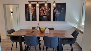 Un espace repas comprenant une table en bois, six chaises et trois luminaires fixés au mur.