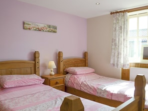 A bedroom with two wooden beds, a nightstand with a lamp, a floral painting on the wall, and a window with curtains. - 3 bedroom accommodation in Brandesburton, near Bridlington (Brandesburton, near Bridlington)