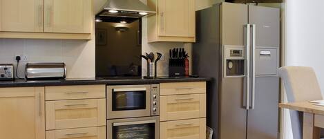 Une cuisine avec des meubles de rangement en bois, un four encastré, un réfrigérateur en acier inoxydable et un grille-pain.