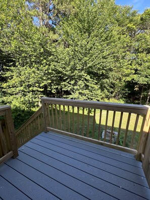 A wooden deck with a railing, surrounded by lush green trees.