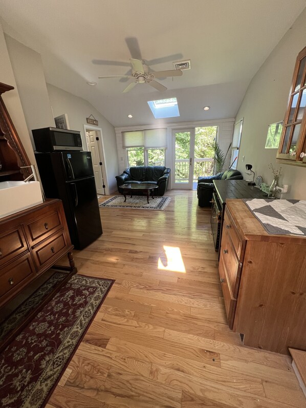 A spacious kitchen with a refrigerator, microwave, and wooden cabinets. There is a ceiling fan, a dining table with chairs, and a window with blinds.