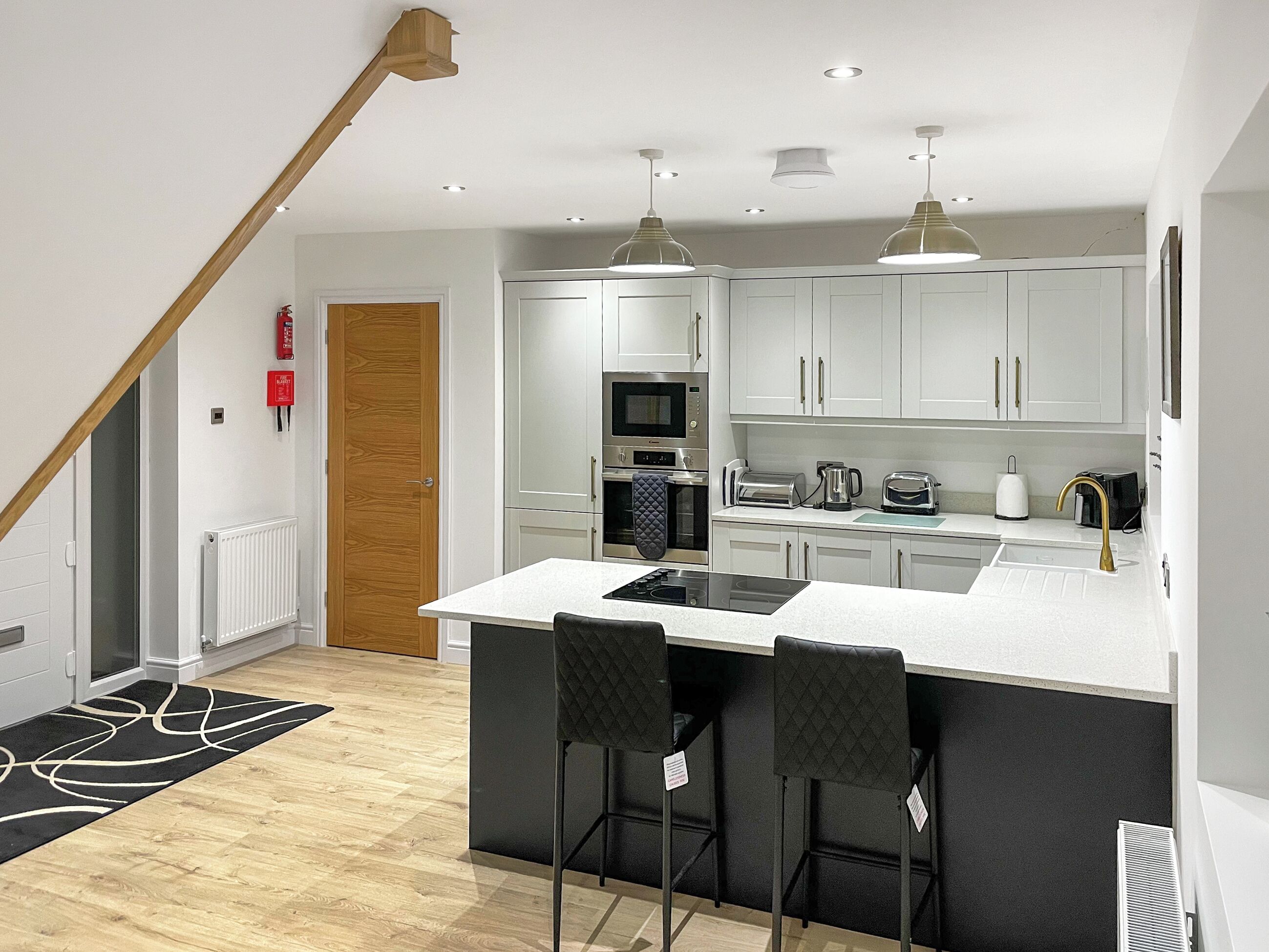 A modern kitchen with white cabinets, a central island, black bar stools, and stainless steel appliances.