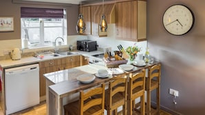 Una cocina moderna con armarios de madera, lavavajillas integrado, zona de comedor con sillas de madera y un reloj de pared.