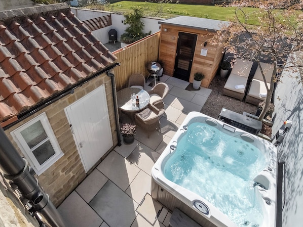 Un jacuzzi, mobiliario de jardín y un cobertizo pequeño en un patio trasero.