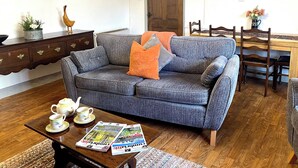 Una sala de estar con un sofá gris, una mesa de centro de madera y un comedor con una mesa y sillas de madera.