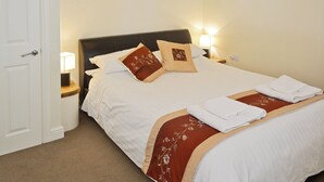 A neatly made bed with white linens and brown decorative pillows, a bedside lamp, and a framed picture on the wall.