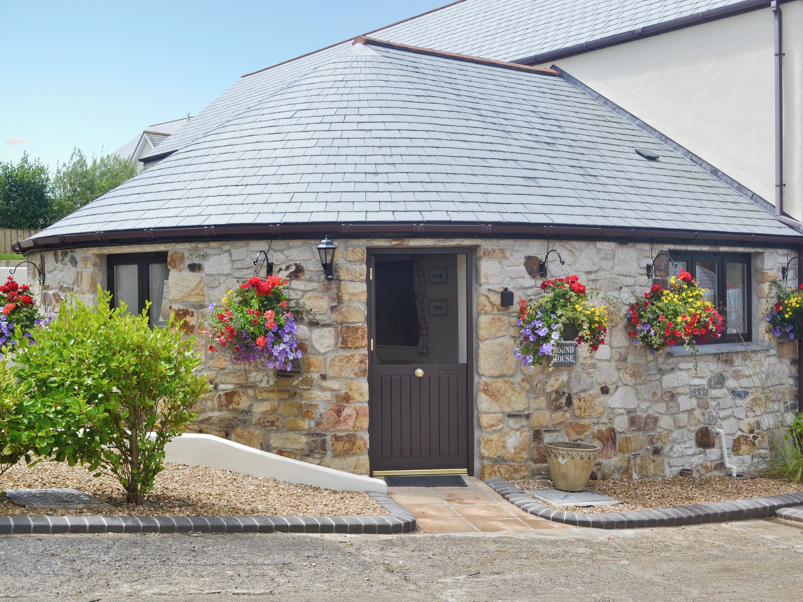 A stone building with a dark roof, a door, and flower baskets on the windowsills.