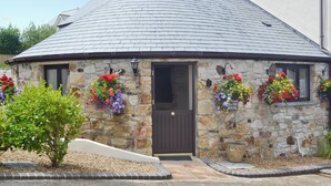 A stone building with a dark roof, a door, and flower baskets on the windowsills.
