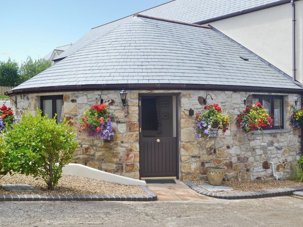 A stone building with a dark roof, a door, and flower baskets on the windowsills.