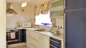 A compact kitchen with a microwave, oven, sink, and a window with floral curtains.