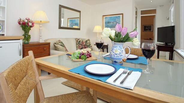 A dining area with a table set for two, a vase with flowers, a television, and a painting on the wall. - 1 bedroom accommodation in Frant, Tunbridge Wells (Frant, Tunbridge Wells)