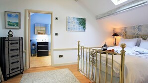 Une chambre à coucher avec un lit, une table de chevet, une lampe et une vue sur la salle de bain par une porte ouverte.