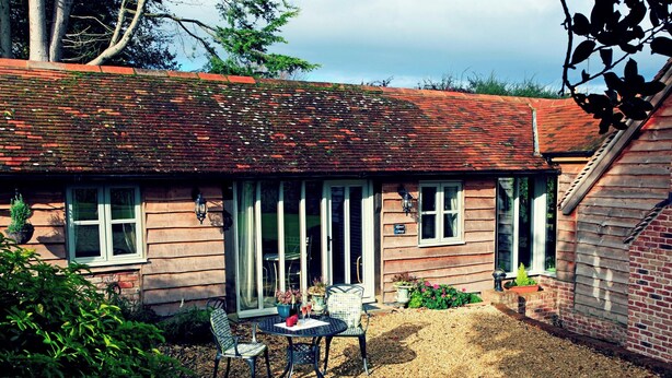 Une petite maison en bois avec une terrasse en gravier, deux fenêtres et un petit jardin.