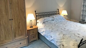 Une chambre à coucher avec un lit, deux tables de chevet avec des lampes, une armoire en bois et une fenêtre avec des rideaux.