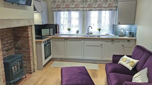 Une cuisine compacte équipée d’un four à micro-ondes, d’un grille-pain et d’une cuisinière, ainsi qu’un canapé violet et une cheminée.