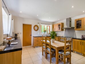 Una cocina moderna con armarios de madera, una mesa de comedor con sillas, un reloj en la pared y una ventana con vistas a zonas verdes.