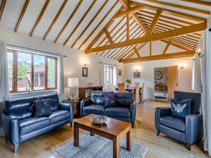 A spacious living room with leather sofas, a wooden coffee table, and a high ceiling with exposed beams.