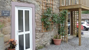 A stone building with a wooden balcony, a potted plant, and a sign reading "Barn Owl Bothy". - 0 bedroom accommodation in Brocklebank, near Caldbeck and Uldale (Brocklebank, near Caldbeck and Uldale)