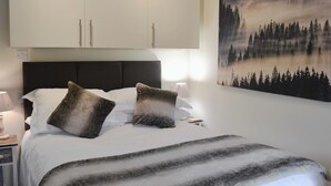 A neatly made bed with a white and gray striped blanket, two pillows, and a headboard. A painting of a forest with a misty lake is on the wall to the right. - 0 bedroom accommodation in Brocklebank, near Caldbeck and Uldale (Brocklebank, near Caldbeck and Uldale)